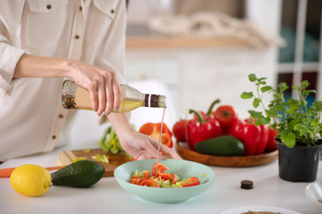 Female hands holding a bottle of vegetable oil over a plate.