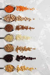 spoons with different cereals are laid out in an even row on the table. orange, black and white cereals