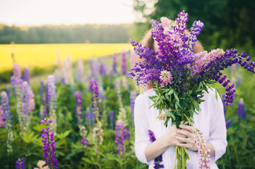 Beautiful woman in a white dress hid her face behind a large bouquet of lupins