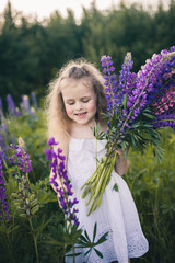 Cute baby in a white dress holds a large bouquet of flowers in nature