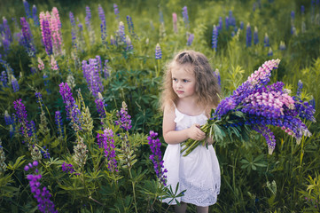 Cute baby in a white dress holds a large bouquet of flowers in nature