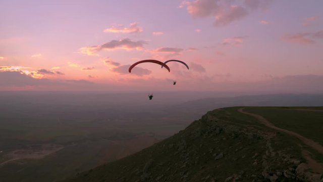 Two paragliders fly over mountain top in epic pink sunset light. Parachutes or paragliding experience. Adrenaline and extreme sport. Beautiful tranquil and calm time in nature