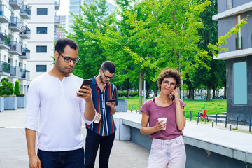 Group of people in casual using mobile phones outside. Two men texting messages, smiling woman talking on cell. Gadget using concept