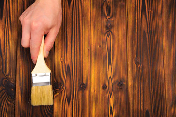 hand holding a brush over can of paint on a wooden table - Image