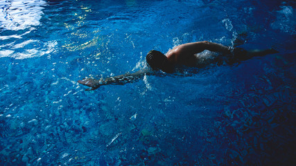 Professional male swimmer crawls underwater in a blue swimming pool
