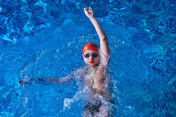 Joyful smiling boy swimmer in a cap and Goggles learns professional swimming in the swimming pool...