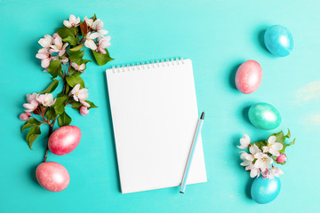 Festive Easter layout with pink Apple tree twigs, colored eggs, white blank notepad with pen on...
