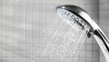 Shower head with running water in white bathroom