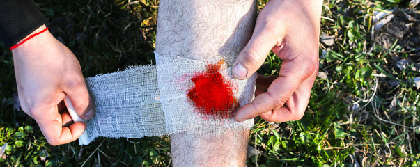 Man is putting bandage on bleeding wound. Injured leg. Tourist in the nature. Infection danger....