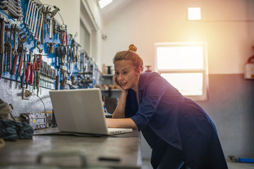 Portrait of a young female mechanic using a laptop. Female mechanic using laptop in a workshop. Business woman at a factory. Craftswoman working using a laptop in the garage.