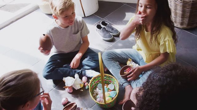 Group Of Children Sitting On Floor At Home Eating Chocolate Eggs They Have Found On Easter Egg Hunt
