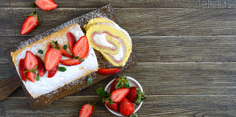 Sweet biscuit roll with strawberries and cream on a wooden background. Top view. Banner