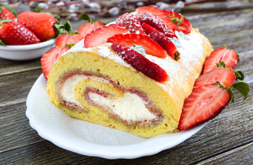 Sweet biscuit roll with strawberries and cream on a wooden background.