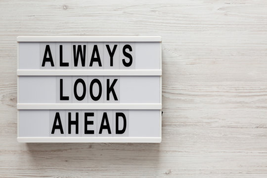 'Always look ahead' words on a modern board on a white wooden background, top view. Overhead, from above, flat lay. Copy space.