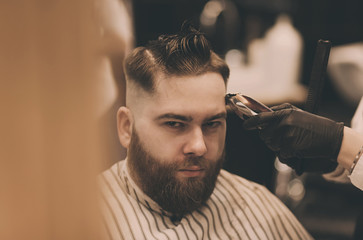 Young man with trendy haircut at barber shop. Barber does the hairstyle and beard trim