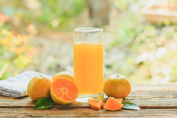 A glass of orange juice and citrus fruits on a wooden table