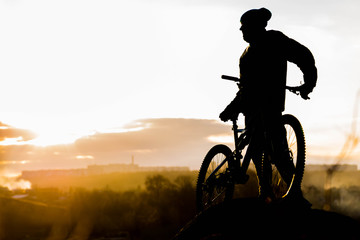 Mountain biker standing on top of a mountain with a bicycle, a beautiful sunset. Silhouette of a cyclist.