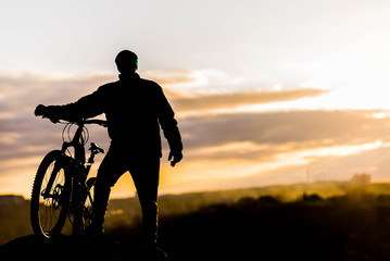 Obraz na płótnie Canvas Mountain biker standing on top of a mountain with a bicycle, a beautiful sunset. Silhouette of a cyclist.