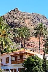 Fototapeta na wymiar Residential home with woodcrafted balcony balustrade in colonial style in front of mountain and palm trees (La Gomera, Spain)