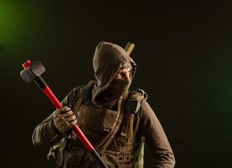 Fototapeta premium a soldier-saboteur rebel in military clothing with a weapon on a dark background holding a sledgehammer