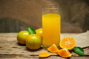 A glass of orange juice and citrus fruits on a wooden table
