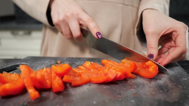 housewife with red manicure cuts Bell pepper on black cutting board making salad for lunch extreme close view slow motion