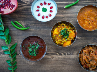 Top down view of some authentic freshly cooked Indian Thali curries on a rustic wooden surface.