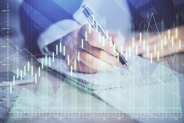 A woman hands writing information about stock market in notepad. Forex chart holograms in front....