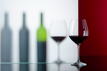 Bottles and glasses of red wine on a black reflective background.