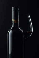 Closed bottle and glass of red wine on a black background.