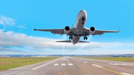 Fototapeta premium Biały samolot pasażerski leci nad pasem startowym z lotniska