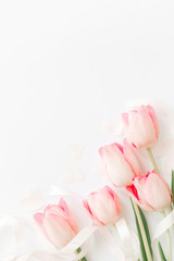 Pink tulips with ribbon and hearts on white background, flat lay. Stylish soft vertical image....