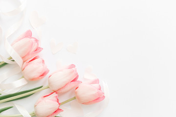 Obraz na płótnie Canvas Pink tulips with ribbon and hearts on white background, flat lay. Stylish soft spring image. Happy womens day. Greeting card mockup with space for text. Happy Mothers day. Hello spring