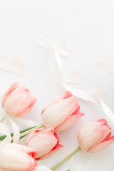 Pink tulips with ribbon and hearts on white background, flat lay. Stylish soft vertical image. Happy womens day. Greeting card mockup with space for text. Happy Mothers day. Valentines day