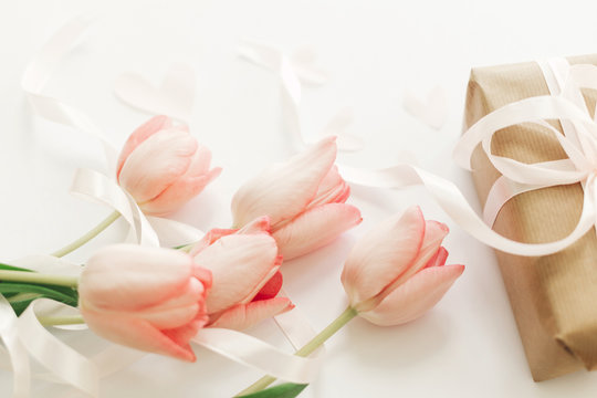 Pink tulips with ribbon and gift box on white background. Stylish soft image of spring flowers. Happy womens day. Greeting card mockup. Happy Mothers day. Hello spring