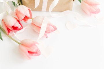 Happy Mothers day.  Pink tulips with ribbon and gift box on white background, space for text. Stylish soft image of spring flowers. Happy womens day. Greeting card mockup. Hello spring