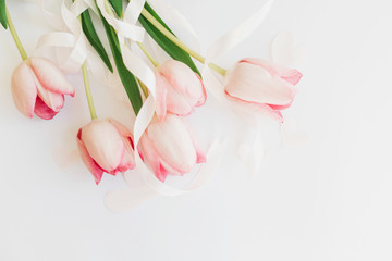 Happy womens day. Pink tulips with ribbon and hearts on white background, flat lay. Stylish soft spring image. Greeting card mockup with space for text. Happy Mothers day. Hello spring