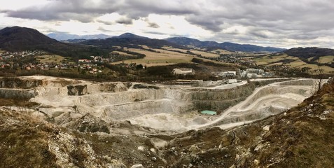Panorama of the giant limestone pit. Thousands birches on the cliffs and bottom of the pit. Summer colors. Blue dramatic sky with clouds. Extraction of minerals in the open way. Mine craft
