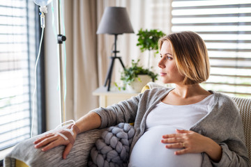A portrait of pregnant woman with IV drip indoors at home or in hospital.