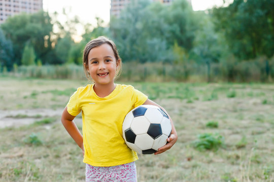 Outdoor photo of cute little girl leaning on soccer ball in green grass