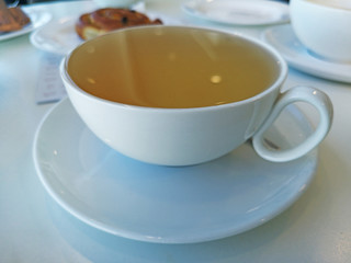White cup with green tea on white table.