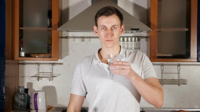 tall young man pours water into glass from bottle and drinks assuaging thirst and standing at table with vegetables close up