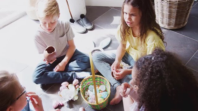 Group Of Children Sitting On Floor At Home Eating Chocolate Eggs They Have Found On Easter Egg Hunt