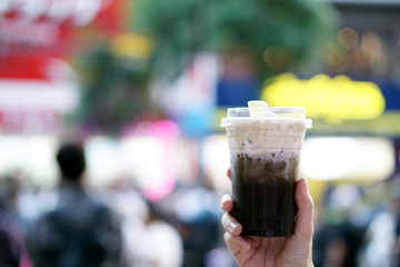 Hojicha milk tea - Hand holding plastic glass of iced milk tea with layer of cream cheese foam on blurred background and copy space, Traditional Taiwanese drink.