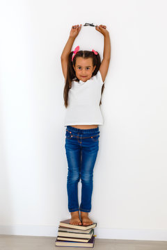 Little girl measuring height against wall in room