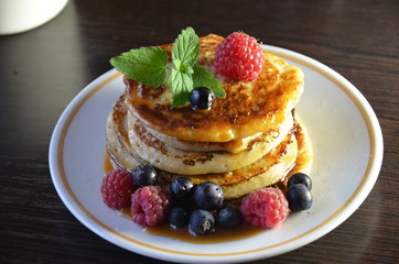 Pancakes with berries and maple syrup with raspberries and blueberries on a black background