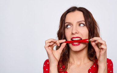 Portrait of a pretty girl in red with chili pepper in her mouth.