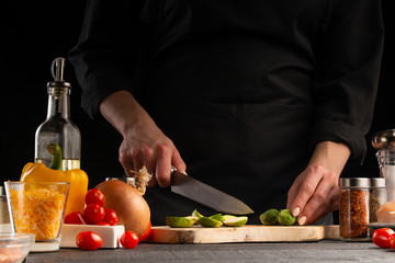 Cook preparing food by the chef, the cook cuts green beans on a background of vegetables. Black background for design, vegetation and proper nutrition.