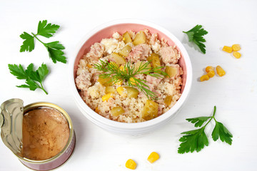 Salad with tuna, couscous, pickled cucumbers and corn, next to a can of tuna in olive oil