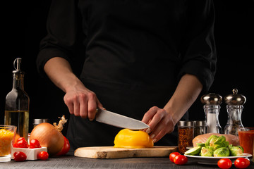 Cooking fresh salad, the chef cuts the paprika on the background of vegetables. Vegetables and healthy eating.